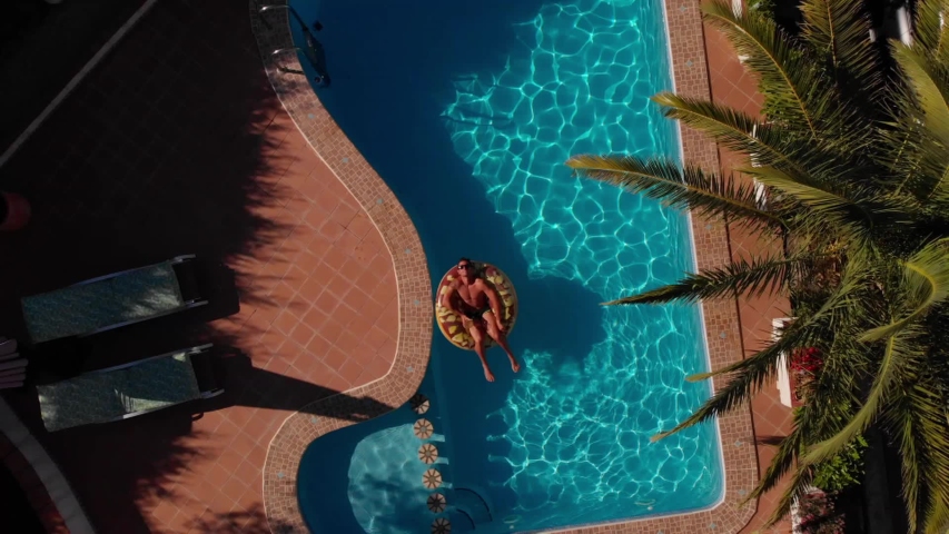 from above a man on beach mat in swimming pool of a villa house in a sunny day
