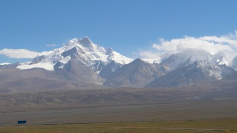 Vast rocky plains lead towards the majestic snow capped mountains in sunny Tibet. Breathtaking view of the scenic Tibetan Plateau and snowy Himalayas on a sunny autumn day. Barren landscape of Tibet.