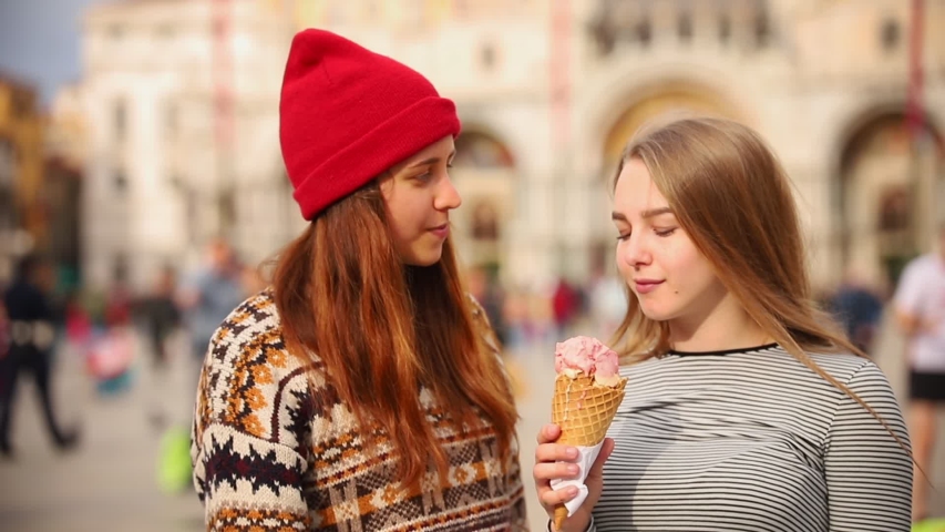 Two women walking at the city square and eat the icecream