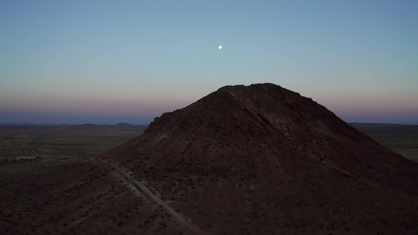 Full moon in purple blue sky over Mojave Desert butte, Aerial Descent