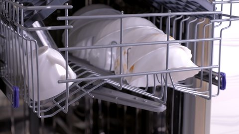 Dishwasher baskets with dirty white dishes and cutlery. Close-up view.