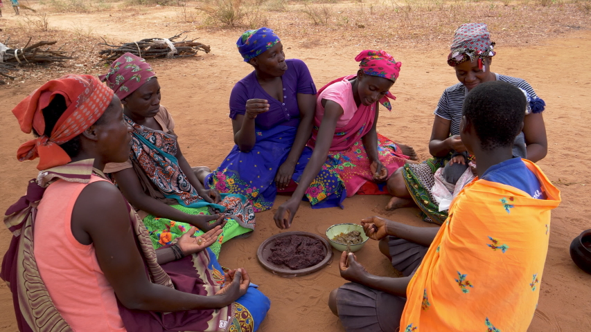 Six woman and a baby sitting on the ground and eating sorghum porridge, Zimbabwe