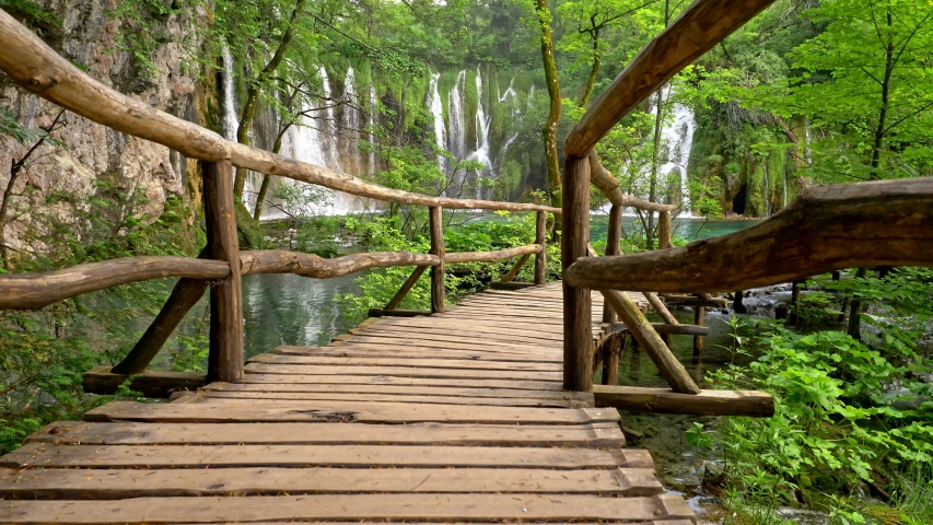 Boardwalk in Plitvice Lakes National Park, Croatia. Transparent turquoise colored waters of the lake are having ripples. Many small waterfalls flowing into the lake. All this surrounded by rich green
