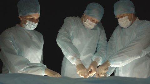 three surgeons, a man and a woman, perform surgery to remove prostate adenoma and varicocele, fibroadenoma, operating theater