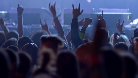 Unrecognizable fans dancing at a concert or festival party. Silhouettes of concert crowd in front of bright stage lights. UHD, 4K , slow motion