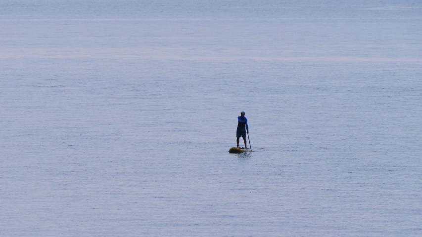 Unrecognizable man riding on stand up paddle board on sea waves at summer time.