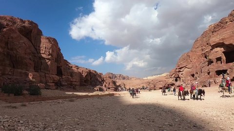 Petra, Jordan November 13 2019: Tourists waving and riding donkeys through ruins of Petra, with ancient Nabatean buildings carved in rocks of the valley.