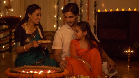 South Indian family dressed in traditional wear is celebrating Diwali at home - Happy Family. Family spending time together, eating sweets and celebrating Diwali - Festive colorful background with ...
