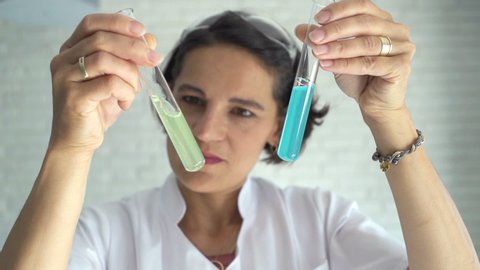 Woman scientist looking at chemicals in test tube at lab, slow motion