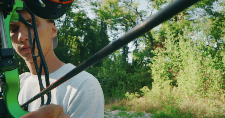 Slow motion close up of young man with professional equipment is practising archery with a bow in a woods in a sunny day. 