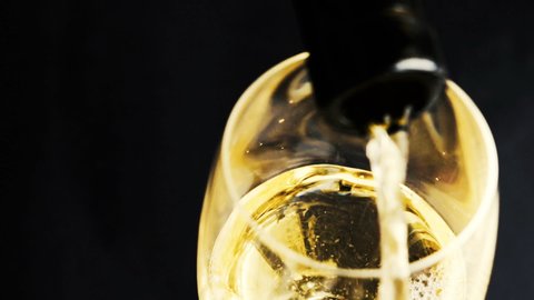 Pouring white wine into wine glass. Closeup of wineglass and bottleneck against black background. 
