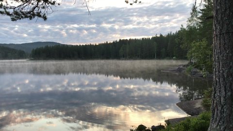 4K video of fog mist drifting over beautiful and calm lake fjord during sunrise golden hour in Maridalen in Oslo, Norway.