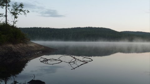 4K anamorphic video of fog mist drifting over beautiful and calm lake fjord during sunrise golden hour in Maridalen in Oslo, Norway.