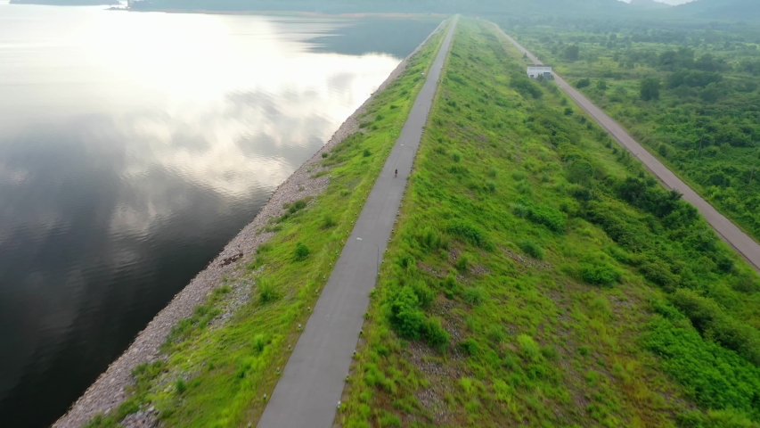 Aerial drone footage. A young athlete rides a healthy exercise bike. In the countryside on the embankment, there are beautiful views of the trees and the lake. Tracking shot
