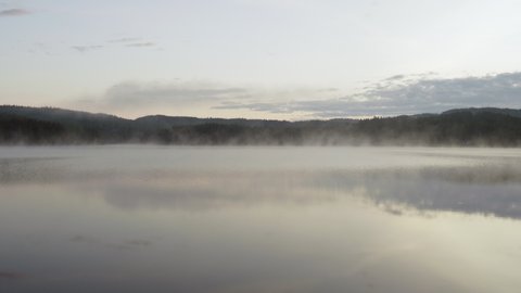 4K anamorphic video of fog mist drifting over beautiful and calm lake during sunrise golden hour in Maridalen in Oslo, Norway.