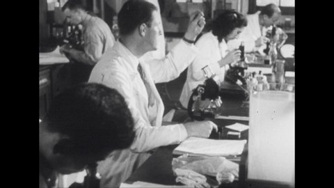 1950s: Row of doctors in lab looking into microscopes. Rows of doctors at work at tables in lab. Man sits in front of industrial calculator.