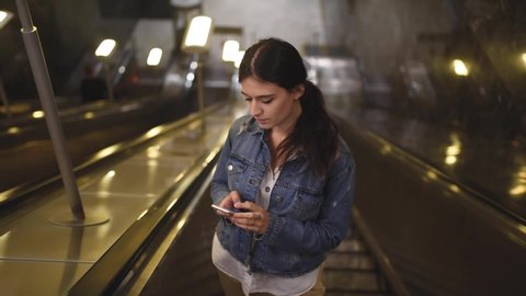 Girl in denim jacket riding the escalator in the subway and scrolling the phone