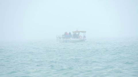 A lone motor boat with tourists or fishermen moves on the waves in the open sea in cloudy foggy weather.