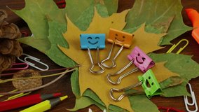 Smiles Binder Clips on Yellow Fallen Maple Leaves and School Office Supplies on brown wooden table. Concept of back to school or education in the fall in September or October