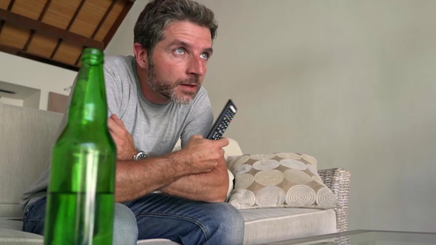 young attractive nervous and stressed man watching football game on television excited bitting his fingernails  sitting at home living room couch feeling the stress and emotion of sport competition 