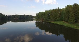 4K aerial summer early morning high quality video footage of pristine lush green pine tree surrounded forest lake with calm water reflecting clouds, a dam, island, sand beach at small town in Russia