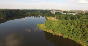 4K aerial summer early morning high quality video footage of pristine lush green pine tree surrounded forest lake with calm water reflecting clouds, a dam, island, sand beach at small town in Russia