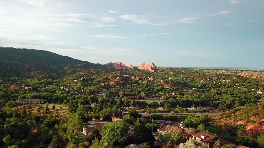 Aerial, drone shot, over buildings and a road, at the at the Garden of the Gods park, red sandstone mountains, in the background, on a sunny evening, in Colorado springs, USA