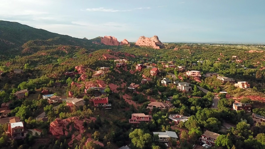 Aerial, drone shot, over buildings towards red sandstone mountains, at the Garden of the Gods, at sunset, on a sunny evening, in Colorado springs, USA