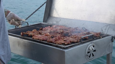 Fethiye, Turkey - 11th of July 2019: 4K Sunset tour on the board of Seaside - Cooking chicken chops on grill at the sea
