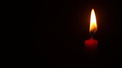 Close Up Red Candle on black background. Yellow flame waving in the night. Romantic and elegant wax candle goes out in the wind. Copy space  Right aligned content. Commemoration, anniversary concept