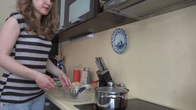 Beautiful housewife girl take boiled spaghetti from pot to glass dish in kitchen. Static shot. 4K UHD video clip.