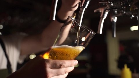 Bartender pouring beer into glass with bubbles close up
