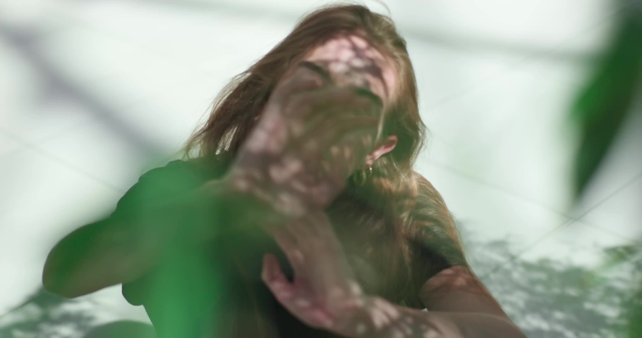 Beautiful girl with green eyes between green branches of trees. The charming look of the beautiful girl