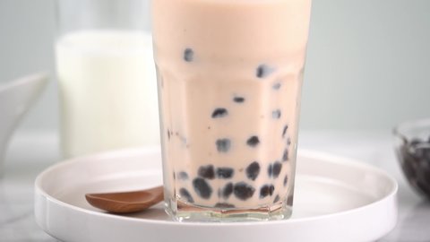 Slow motion - Stirring tapioca pearl bubble milk tea in drinking glass, tasty taiwanese popular drink on bright marble table. Homemade concept.