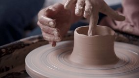 Concentrated adult ceramist person working with wet clay and standing inside small craft studio. Qualified, skilled and confident woman spending time in work space with natural light