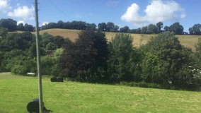 Wide shot out of a window of train, tracking along flat british UK southern England countryside and farmland clouds and blue sky - stock footage video