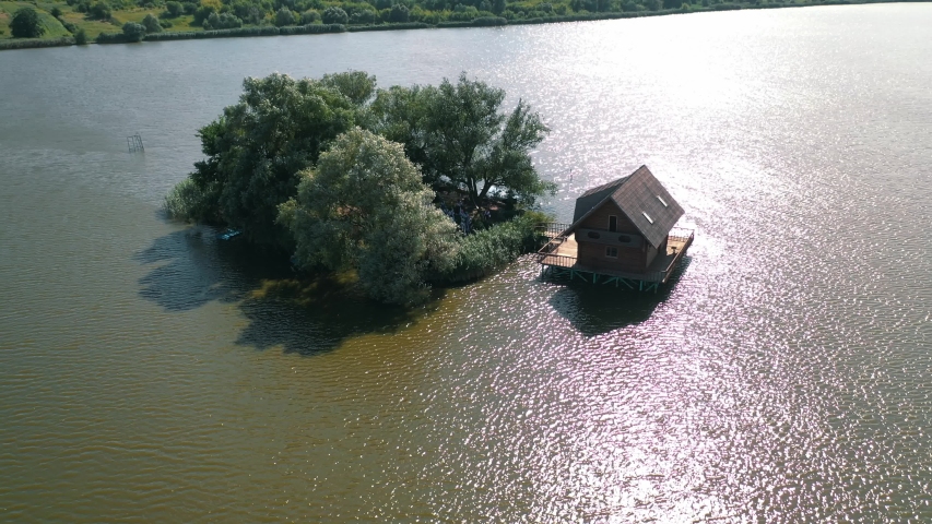Small island and a house in the middle of the river. Aerial view of beautiful green island surrounded by water. Camera moves round.