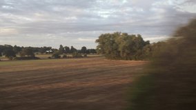 Wide shot out of a window of aing train, tracking along flat british countryside and farmland
