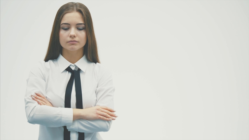 Young pretty business girl standing on a white background. During this, he looks into the camera by placing his hands in his pockets.