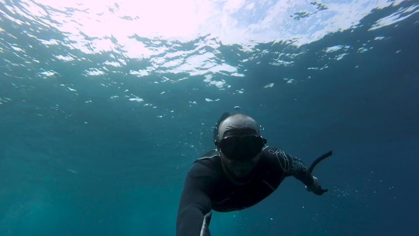 White male freediver with beard does 360 degree barrel roll while holding a selfie stick in blue tropical waters with sunlight behind him Royalty-Free Stock Footage #1033619756