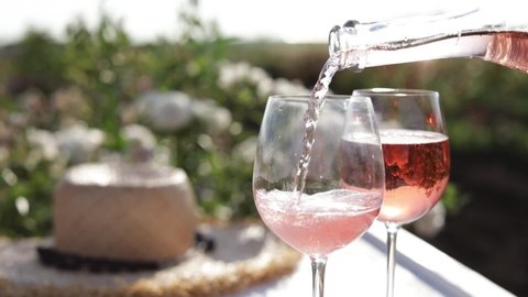 Pouring rose champagne into glass in garden on sunny day, closeup. Space for text
