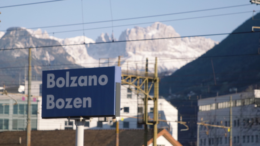 Bolzano train station sign with city name, mountains on the background. Trentino, Italy