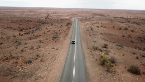 Aerial: Drone shot tracking a vehicle driving down an empty road in the Australian outback towards the horizon near Broken Hill, Australia