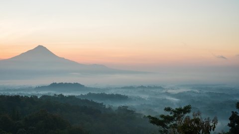 Sun ricing over Mount Merapi, overlooking the Buddhist temple Borobudur, lost in the early morning swirling mist.