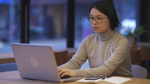 Closeup of Asian woman sitting in coffee, searching for information on laptop, drinking a glass of water. Chinese female looking for message need on computer working in morning.