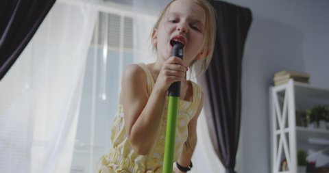 Full shot of girl singing and using mop handle as microphone