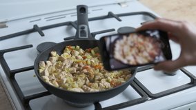 Video kitchen blog. Woman`s hand with a telephone makes a video of fry vegetables with chicken in the fry pan.