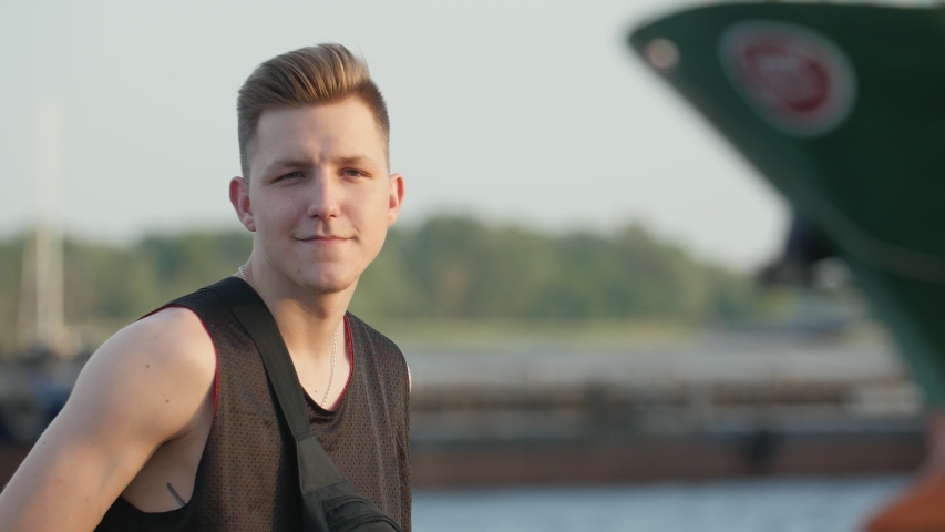 Cheerful portrait of positive blond man with nice hairstyle on the quay at sunset