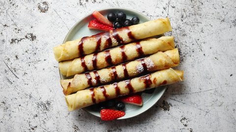 Plate of delicious crepes roll with fresh fruits and chocolate placed on rusty table. Top view, flat lay.