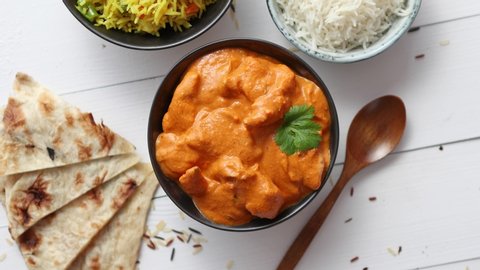 Fresh and tasty Butter Chicken served in ceramic bowl. Indian mild traditional dish. With rice and naan bread on sides. Close up. Flat lay.